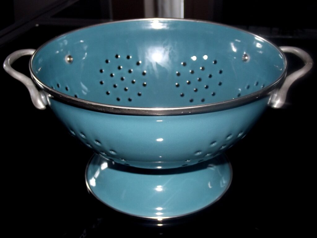 A metal colander seated on the rim of a deep pot with steam rising around the edge