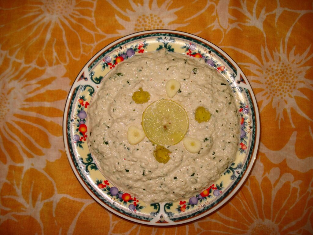 An open jar of pale beige sesame paste with a spoon standing upright in the center