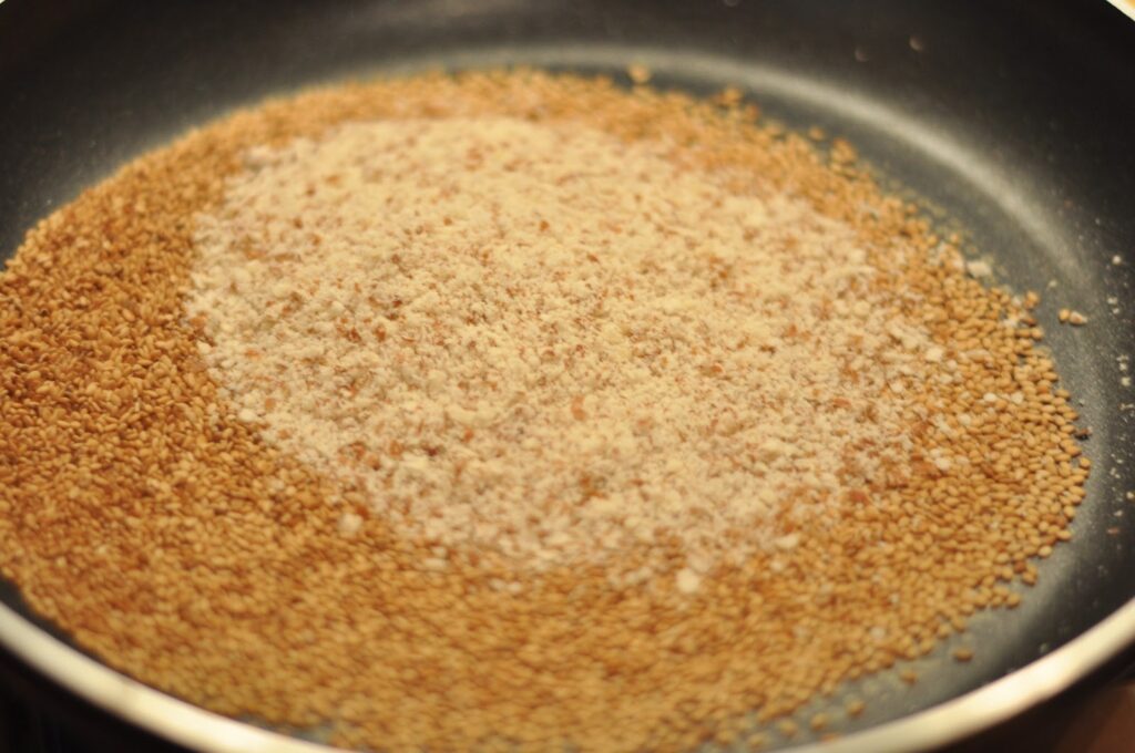 Toasted sesame seeds spread across a dark pan, browned unevenly and still warm