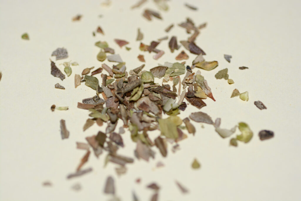 Crumbled dried oregano heaped on a small saucer beside a woody sprig of the herb