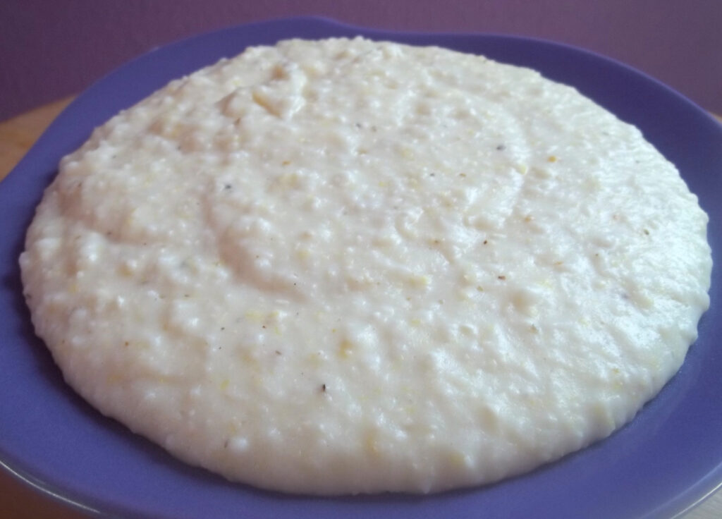 A pale round of elastic brined white cheese on a board beside a knife and crumbs