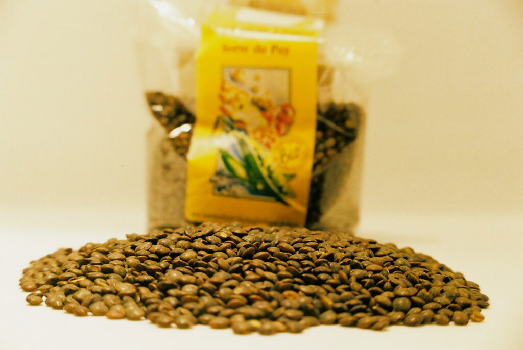 Small slate green mottled lentils gathered in a metal spoon above a linen cloth