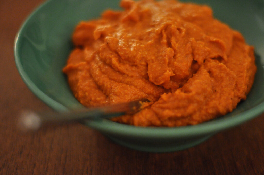 A thick brick red almond and pepper sauce in a small bowl with a spoon resting in it