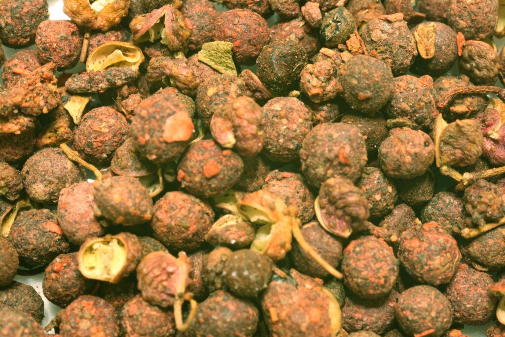 Rust colored husks of Sichuan pepper scattered on a pale dish beside a small grinder