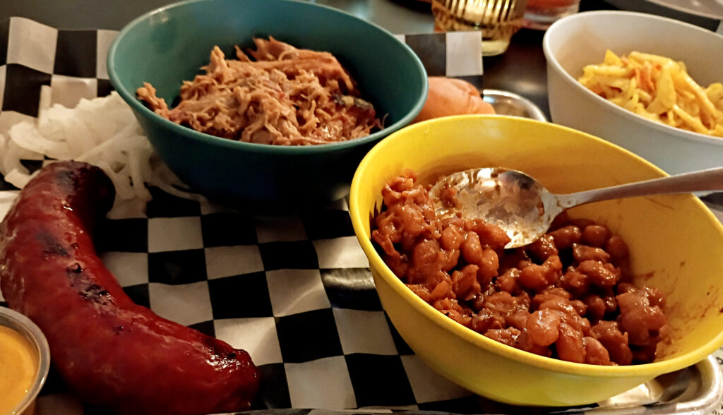 Shredded smoked pork pulled apart with two forks on a board, showing dark bark and pale meat