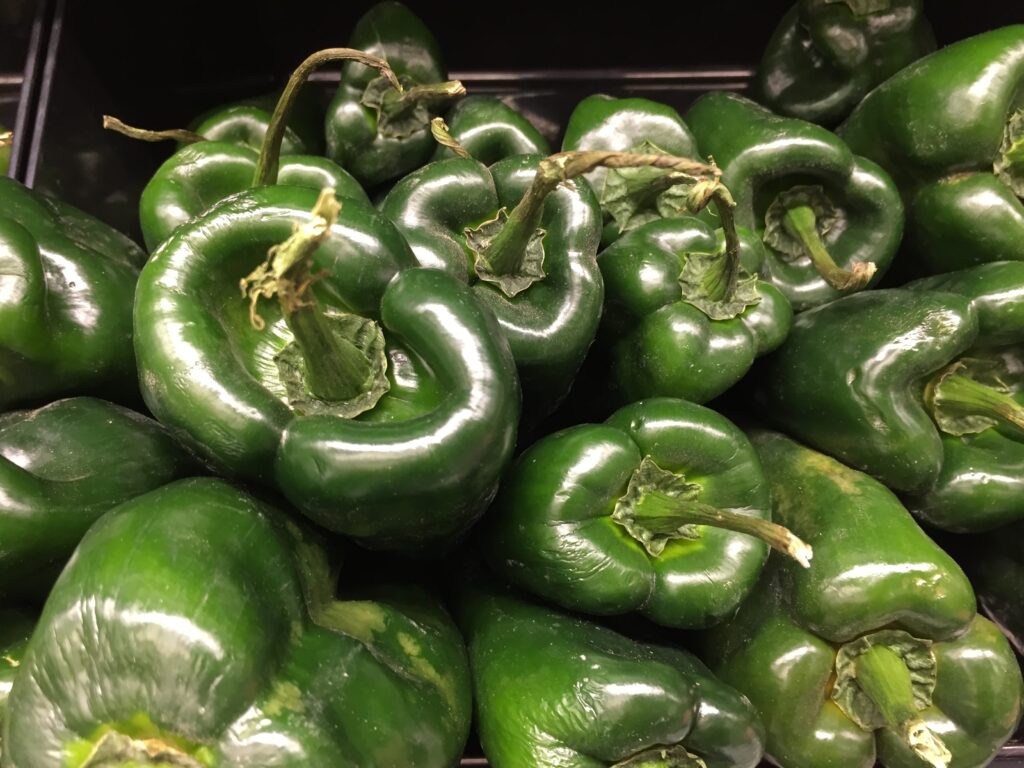 Three dark green wide-shouldered fresh peppers with glossy skins resting in a basket