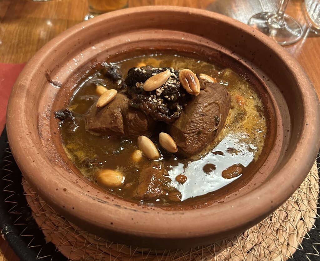 A glazed clay tagine with its conical lid tilted open over braised lamb and onions