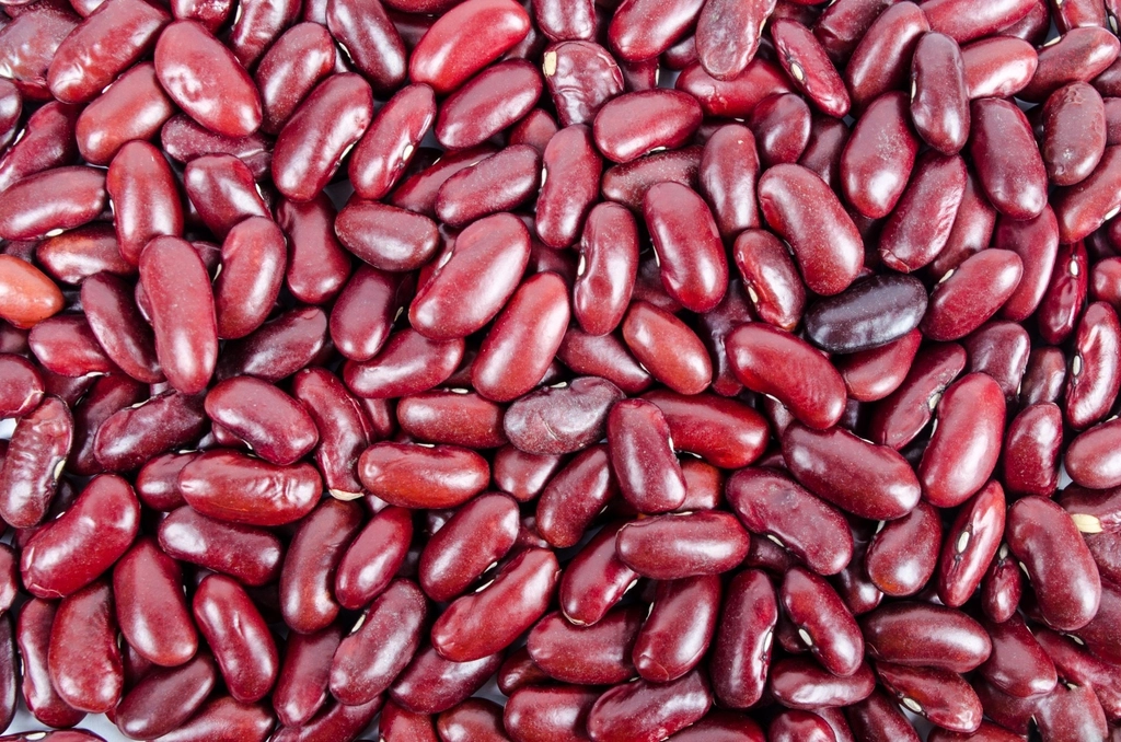 Glossy dark red kidney beans spilling from a cloth sack onto a pale wooden surface