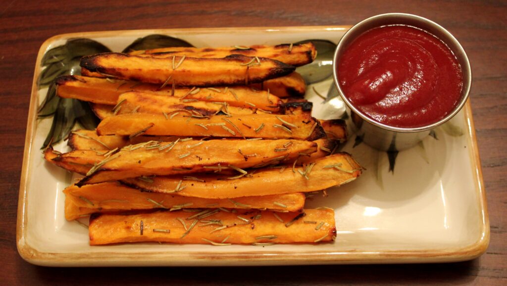 Two split baked sweet potatoes with caramelised syrup at the edges on a metal tray