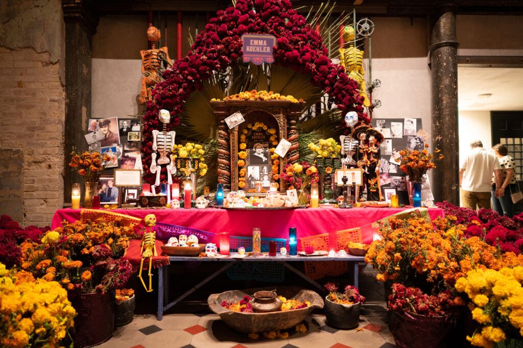 An ofrenda altar with marigolds, candles, framed photographs, and small plates of food