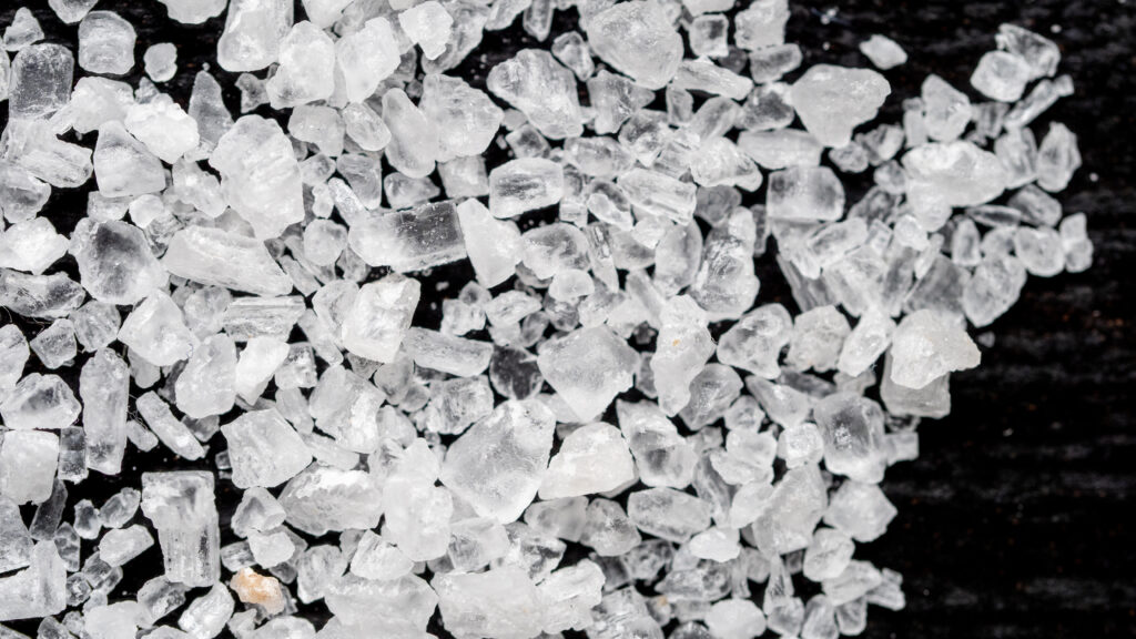 Coarse grey salt crystals piled in a shallow dish with a small wooden scoop