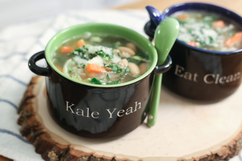 A pot of white bean soup with dark kale leaves stirred through a golden broth